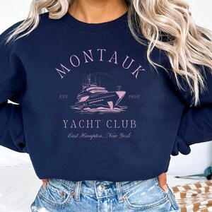 May include: A navy blue sweatshirt with a pink graphic of a yacht and the text "Montauk Yacht Club Est. 1900 East Hampton, New York".