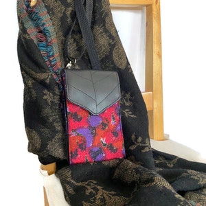 May include: A black crossbody phone bag with a leaf-shaped flap. The bag's body has a vibrant pattern of red, purple, and orange with small illustrations. It has a black strap and a silver clasp.