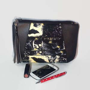 May include: Black and white clutch bag with a skull and raven design. The bag has a zip closure and a tassel. The text "Nevermore" is printed on the bag.