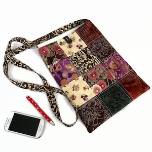 May include: A patchwork fabric crossbody bag with a brown strap. The bag is made of various fabrics with floral and paisley patterns in shades of brown, purple, red, and cream.