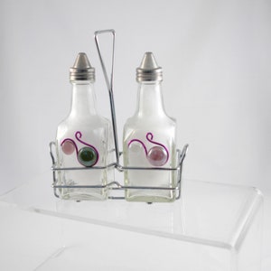 May include: A silver metal salt and pepper shaker holder with two clear glass bottles with pink and green accents. The bottles have a silver metal top.