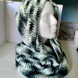 May include: A hooded scarf in a green, white, and black color scheme. The scarf is crocheted and has a striped pattern.