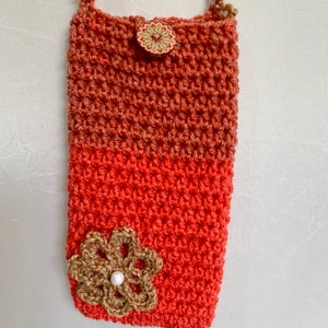 May include: A crocheted purse with a brown strap and a coral and brown color scheme. The purse has a flower embellishment and a button closure.