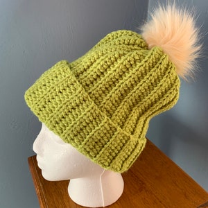 May include: A green crocheted beanie with a fluffy white pom pom on top.