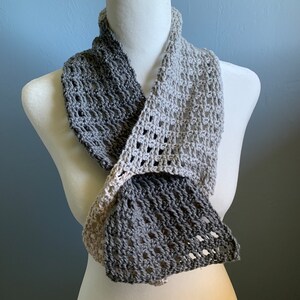May include: A gray and white crocheted infinity scarf with a lacy pattern. The scarf is draped over a white mannequin.