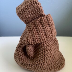 May include: A brown crocheted bag with a folded top and a rounded base. The bag is made of thick yarn, and the stitches are clearly visible. The bag is a solid color and appears to be handmade.