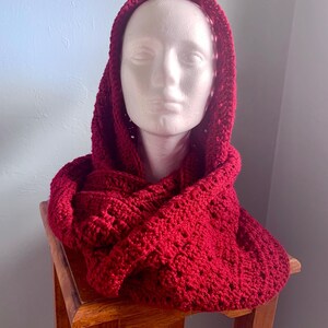 May include: A red crocheted hooded scarf with a lacy pattern.