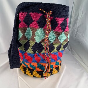 May include: A colorful crocheted tote bag with a geometric pattern in shades of pink, blue, green, yellow, orange, and black. The bag has a long strap and a drawstring closure.