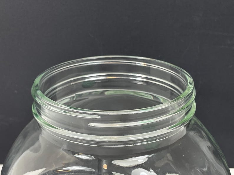 May include: A clear glass jar with a wide mouth and a rounded body. The rim of the jar has a series of concentric rings. The jar is designed for storage and is suitable for various uses.