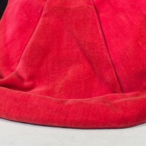 May include: A close-up of a red velvet fabric with a smooth, soft texture. The fabric is folded and draped, creating a rounded shape.
