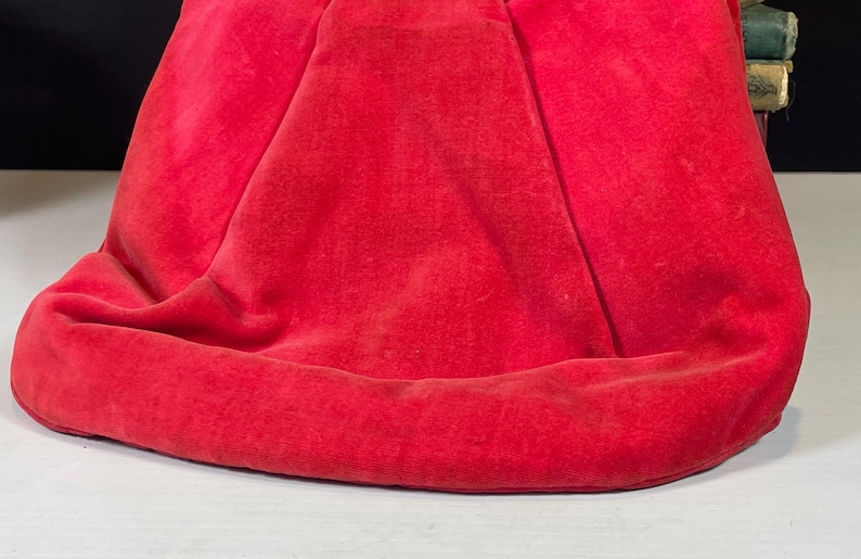 May include: A close-up of a red velvet fabric with a smooth, soft texture. The fabric is folded and draped, creating a rounded shape.