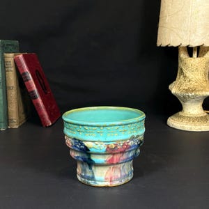 Puede incluir: Un cuenco de cerámica turquesa con un borde texturizado y un diseño multicapa multicolor. El cuenco presenta tonos de azul, rojo y amarillo. El cuenco es un objeto decorativo.