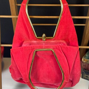 May include: A bright red velvet handbag with a gold metal top handle. The handle is shaped like an oval and has a pointed top.