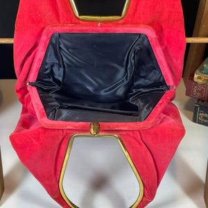 May include: A red velvet vintage clutch purse with a gold metal frame and a black satin lining.