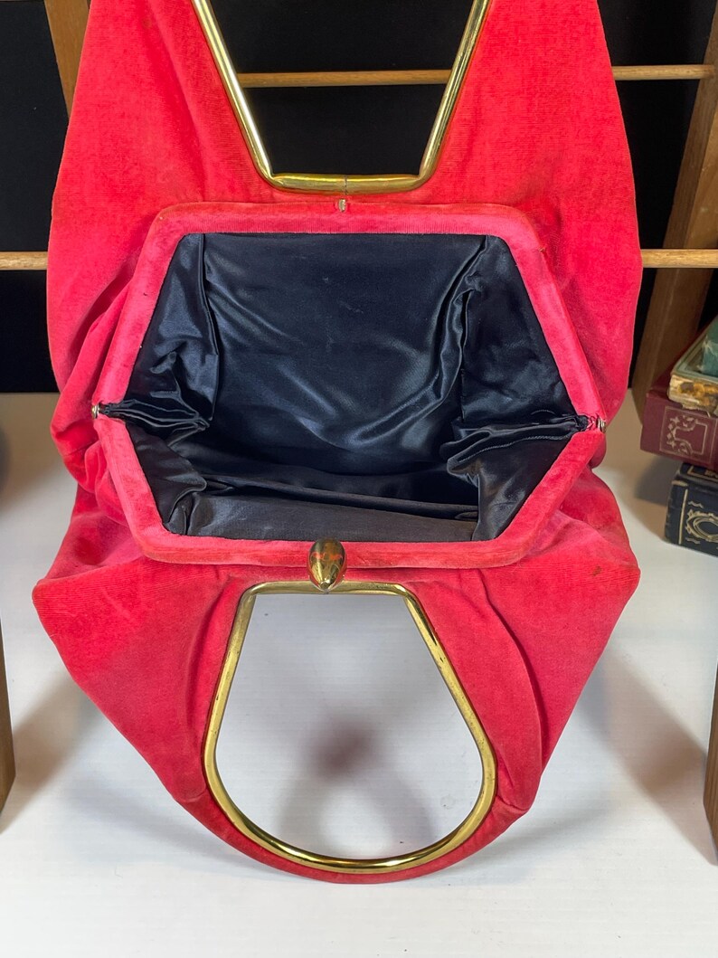 May include: A red velvet vintage clutch purse with a gold metal frame and a black satin lining.