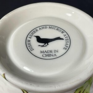 Op de afbeelding: Witte keramische kom met een zwarte vogel afbeelding en de tekst "Dish Washer and Microwave Safe Made in China".