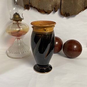 May include: A black and brown ceramic vase with a twisted design and a gold rim. The vase has a rounded base and a wide opening.