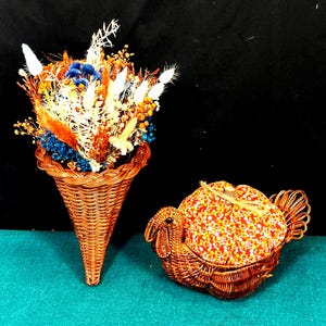 May include: A woven brown wicker cornucopia filled with dried flowers in shades of orange, white, blue, and yellow. A wire turkey-shaped container with a floral patterned lid is next to the cornucopia.