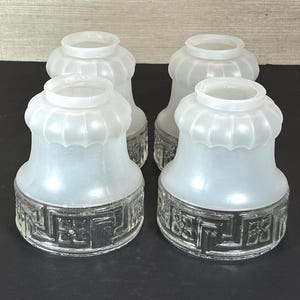 May include: A set of four glass lamp shades featuring a frosted white upper section with a fluted design and a clear lower base decorated with a repeating geometric Greek key pattern and square floral motifs around the circumference.