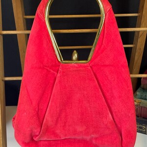 May include: A red velvet handbag with a gold top handle. The handle is a single loop with a rounded top.