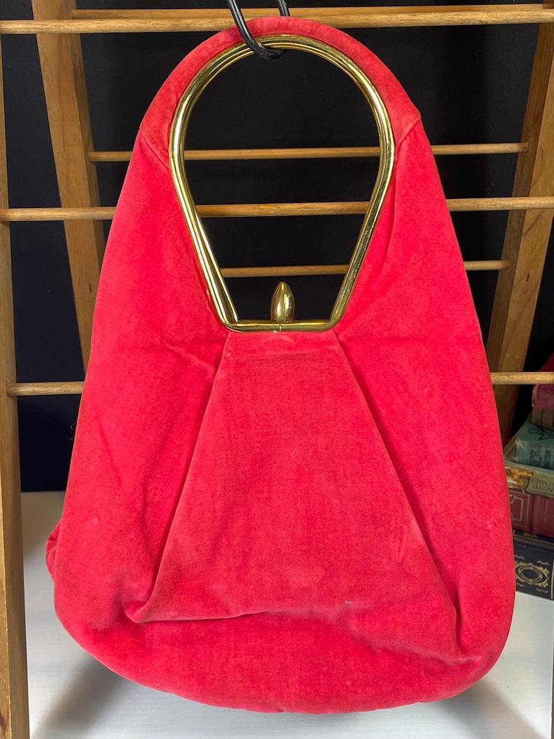 May include: A red velvet handbag with a gold top handle. The handle is a single loop with a rounded top.