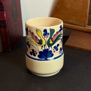May include: A ceramic utensil holder with a cream-coloured base and a blue, green, yellow and red floral design featuring two birds.