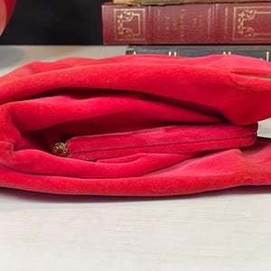 May include: A red velvet clutch purse with a gold clasp. The purse is folded in half and the inside is visible.