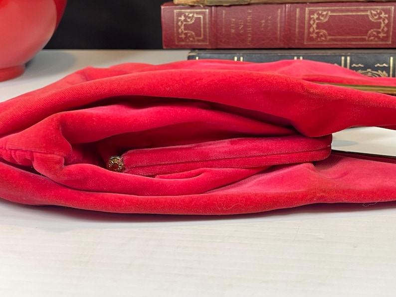 May include: A red velvet clutch purse with a gold clasp. The purse is folded in half and the inside is visible.