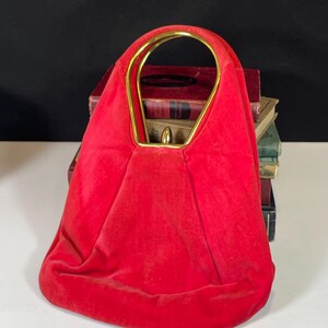 May include: A red velvet handbag with a gold metal top handle. The bag has a rounded shape and a soft, plush texture.