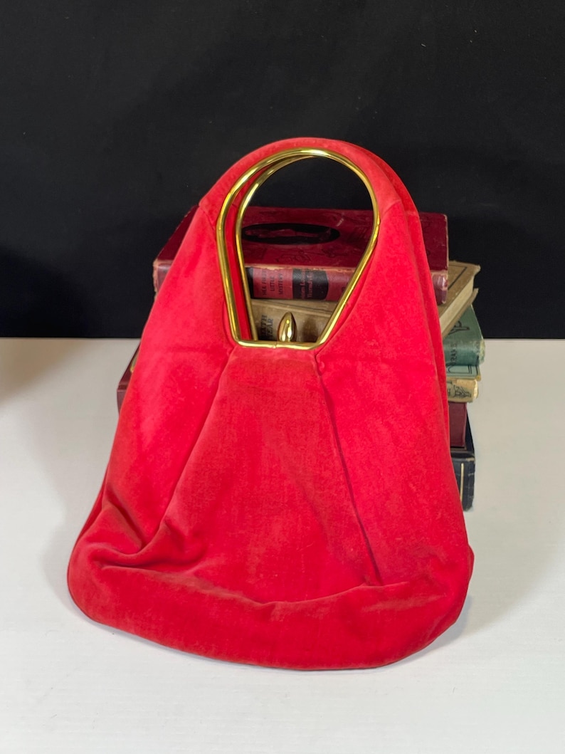 May include: A red velvet handbag with a gold metal top handle. The bag has a rounded shape and a soft, plush texture.