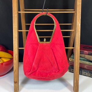 May include: A red velvet handbag with a gold metal frame and a top handle. The bag is hanging on a wooden rack.
