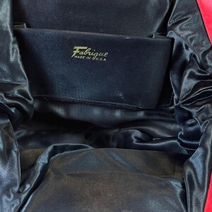 May include: A red velvet evening bag with a black satin lining. The bag has a zipper closure and a label that reads "Fabrique Made in U.S.A."