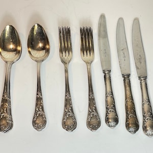 May include: Set of six silver-plated cutlery pieces, including two spoons, two forks, and two knives. The handles are ornate with a floral design. The knives are marked with "WMF" on the blade.