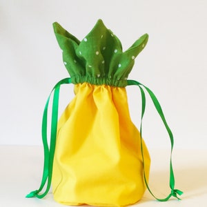 May include: A yellow fabric drawstring bag with a green fabric top with white polka dots. The bag has green fabric drawstrings.