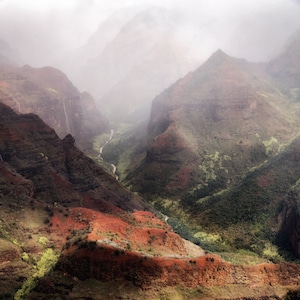 May include: A misty, green valley surrounded by steep, red-brown cliffs. The valley is filled with lush vegetation and a small stream winds its way through the center.