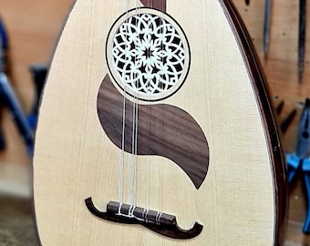 May include: A light wood oud with a dark wood sound hole and a decorative inlay. The oud is sitting on a wooden surface.