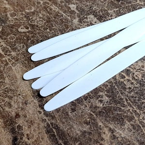 Puede incluir: Un juego de seis púas de guitarra de plástico blanco, dispuestas en forma de abanico sobre una superficie de madera marrón.