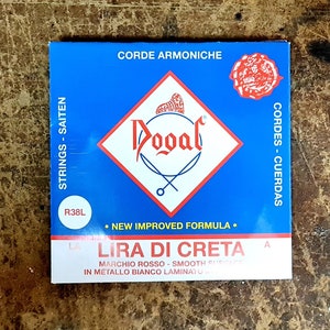 May include: A blue and white package of Dogal Lira di Creta strings for a musical instrument. The package has the text "STRINGS-SAITEN", "CORDE ARMONICHE", "CORDES-CUERDAS", "NEW IMPROVED FORMULA", "LIRA DI CRETA", "MAICHIO ROSSO SMOOTH", "IN METALLO BRANCO LAMINA", and "R38L".