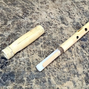 May include: A wooden flute with a removable mouthpiece. The flute is made of light brown wood and has six holes for playing.