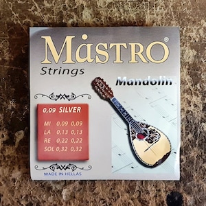May include: A pack of silver-plated mandolin strings by Mástro. The pack features a picture of a mandolin and lists the string gauges: 0.09, 0.13, 0.22, and 0.32. Made in Hellas.
