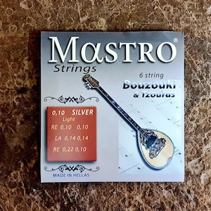 May include: A pack of silver-plated strings for a 6-string bouzouki or tzournas. The pack is white with blue text and a picture of a bouzouki. The text on the pack reads "MASTRO Strings 6 string bouzouki & Tzournas 0.10 SILVER Light RE 0.10 0.10 LA 0.14 0.14 RE 0.22 0.10 MADE IN HELLAS".