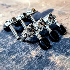 May include: Close-up of three silver guitar tuning pegs with black knobs. The pegs have an ornate design with a silver finish.