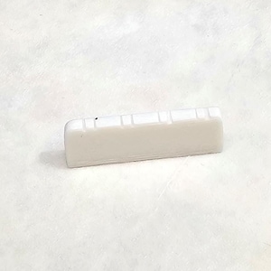 May include: White plastic guitar bridge saddle with six grooves for string placement.