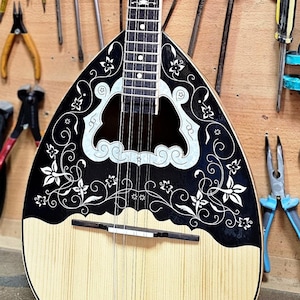 Peut inclure: Un instrument à cordes traditionnel avec un motif floral noir et blanc. L'instrument est exposé contre un mur en bois avec divers outils, notamment des tournevis, des pinces et des pinceaux.