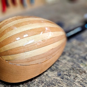 Pode incluir: Um instrumento musical de madeira com um corpo listrado e um pesco&ccedil;o preto. O instrumento est&aacute; sobre uma superf&iacute;cie de madeira.