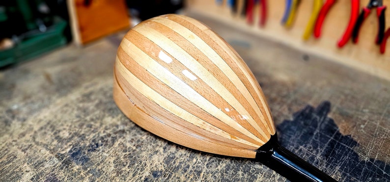 Pode incluir: Um instrumento musical de madeira com um corpo em forma de p&ecirc;ra e um pesco&ccedil;o preto. O corpo &eacute; feito de tiras de madeira clara e escura, criando um padr&atilde;o listrado.