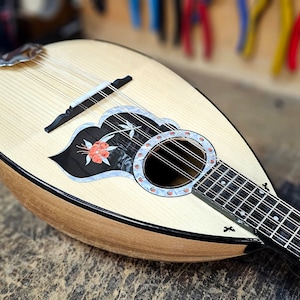Pode incluir: Um bandolim de madeira com um design floral preto e branco na placa de som. O bandolim tem um bra&ccedil;o preto e um acabamento de madeira natural.
