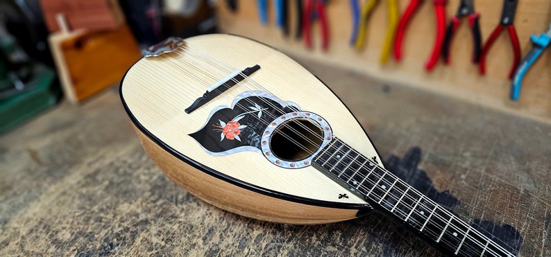 Pode incluir: Um bandolim de madeira com um design floral preto e branco na placa de som. O bandolim tem um bra&ccedil;o preto e um acabamento de madeira natural.