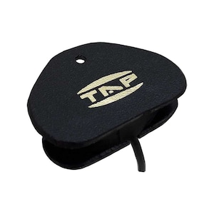 May include: Black leather earpiece with a gold "TAP" logo. The earpiece has a small hole on the top and a cord extending from the bottom.