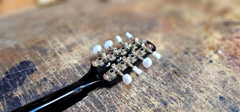 Pode incluir: Close-up da cabe&ccedil;a de um bandolim preto com pinos de afina&ccedil;&atilde;o prateados e bot&otilde;es de pl&aacute;stico branco.